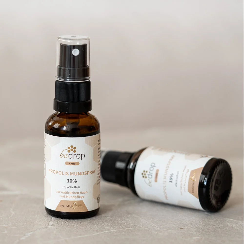 Zwei braune Glasflaschen bedrop Propolis Mundspray 10 % alkoholfrei mit schwarzem Sprühkopf und weiß-beigem Etikett, eine Flasche stehend und eine liegend auf hellem Untergrund.